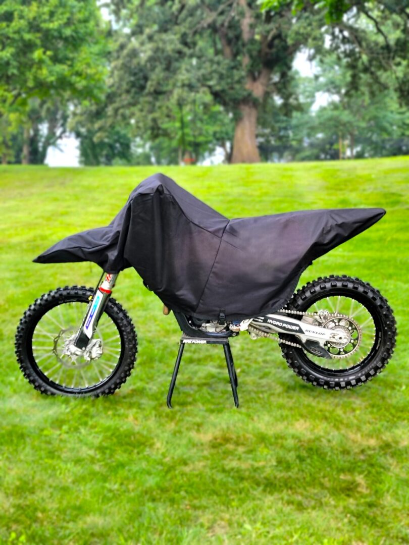 A dirt bike covered with a black protective cover on grass.