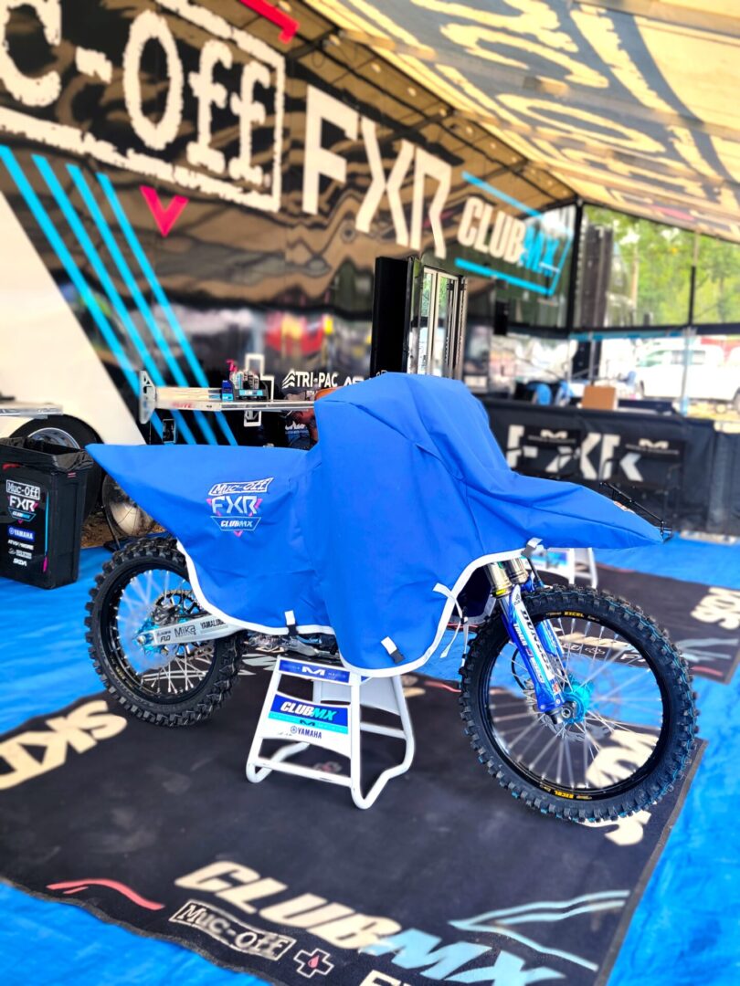 A motocross bike covered with a blue tarp at a racing event.