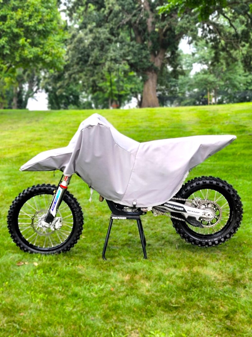 A motorcycle covered with a white protective sheet on grass.