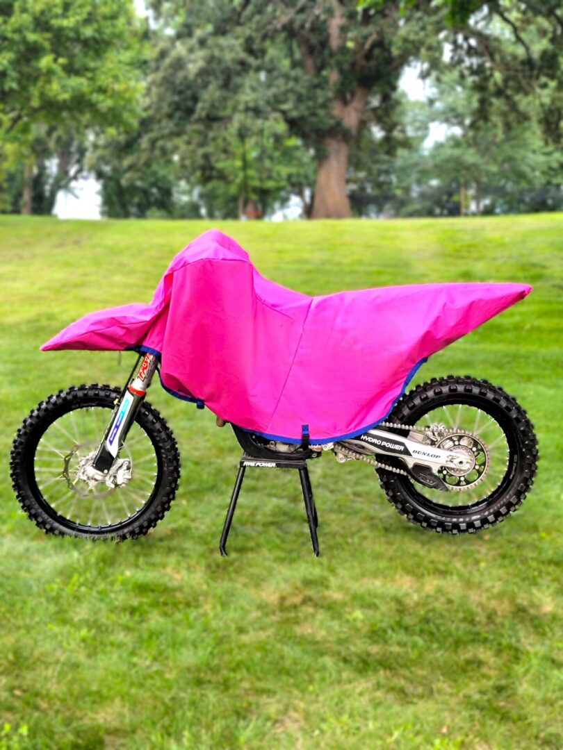 Dirt bike covered with a bright pink protective cover on grass.