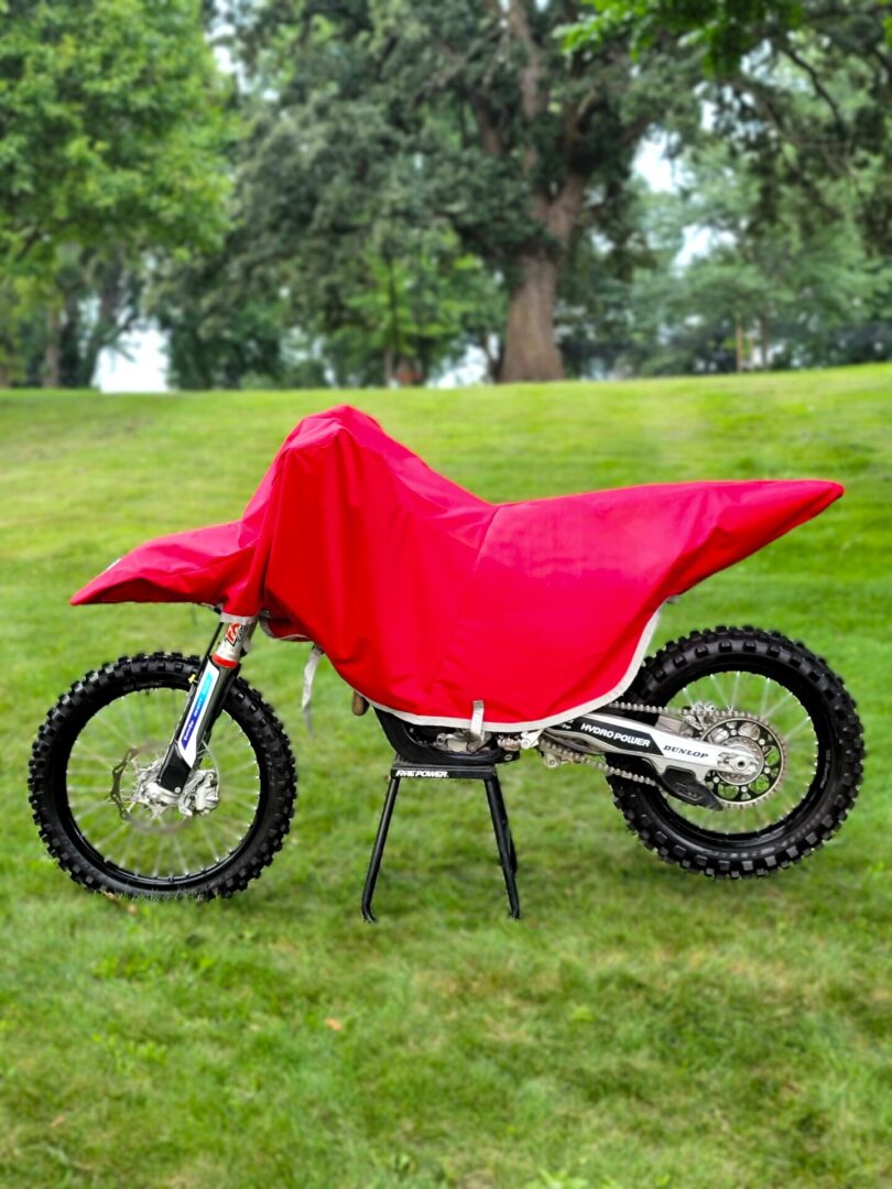 A dirt bike covered with a red cloth outdoors on grass.