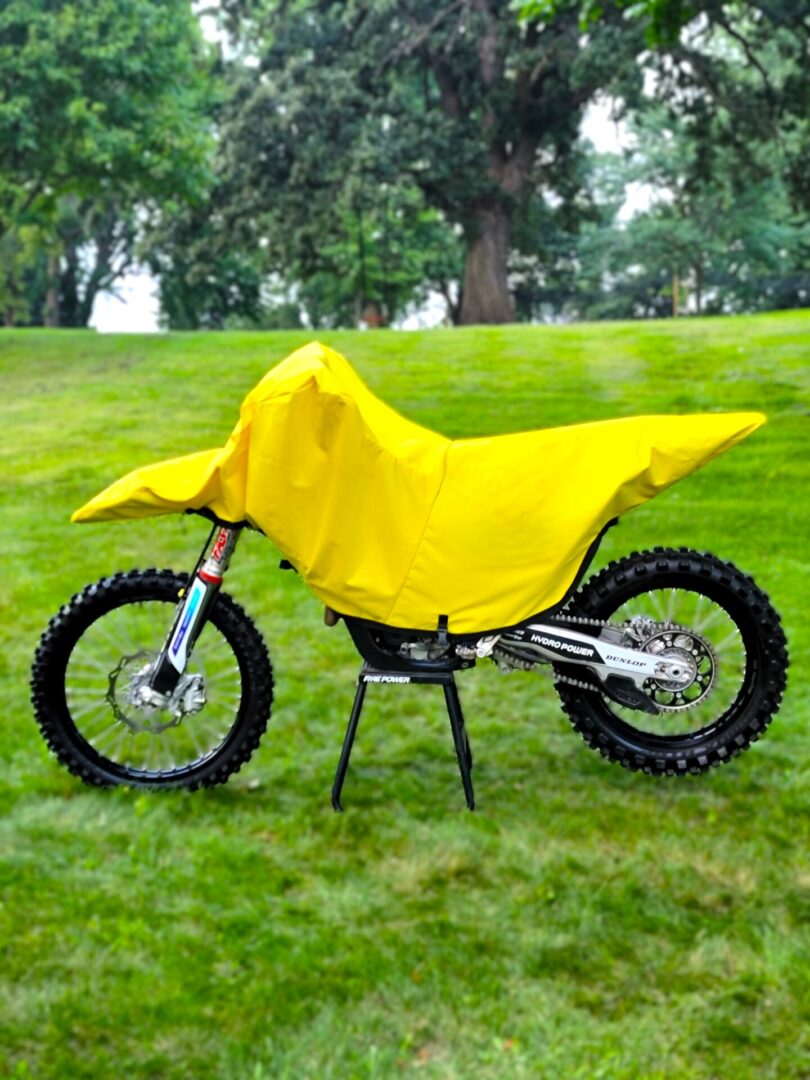 A motorcycle covered with a bright yellow tarp on green grass.